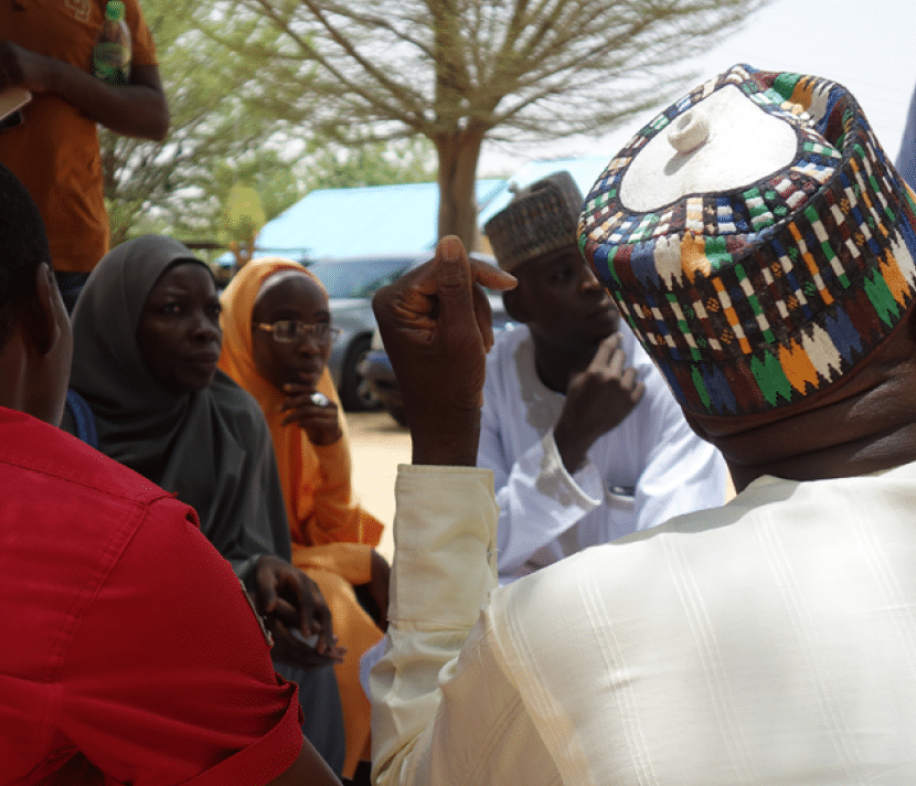 A group of people talking in Nigeria, one man is raising his hand to speak 