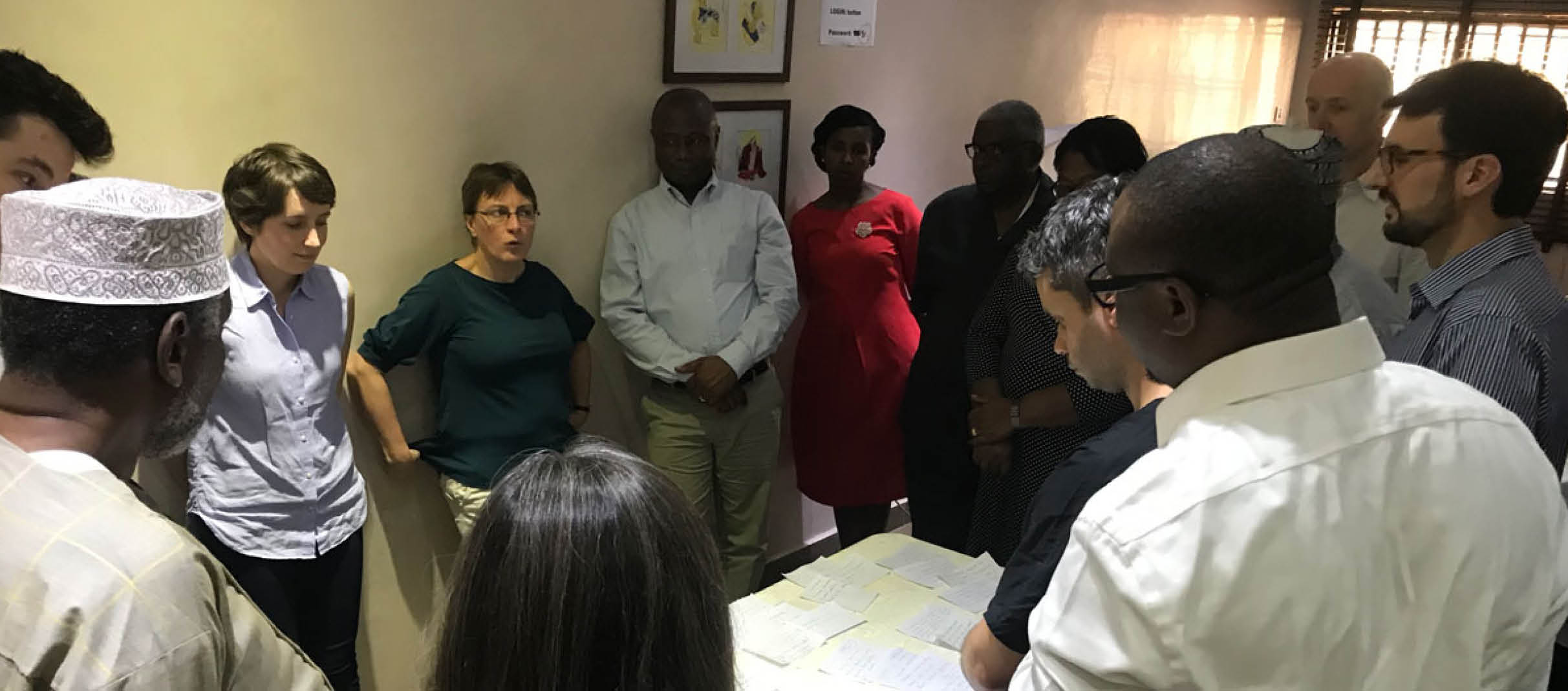 A group in Nigeria are discussing plans on a table, listening to a woman speak