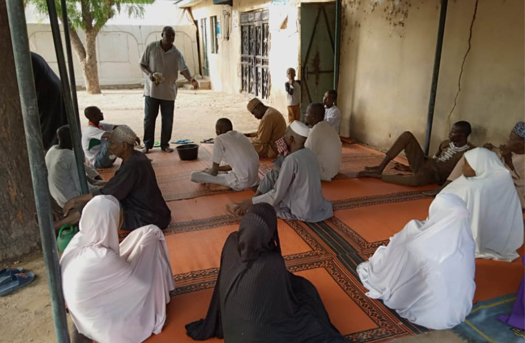 A man speaks to a group of men and women in Nigeria, gesturing openly while the group listen