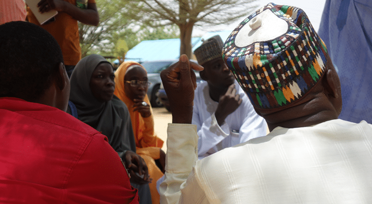 A group of people talking in Nigeria, one man is raising his hand to speak 