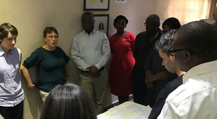 A group in Nigeria are discussing plans on a table, listening to a woman speak